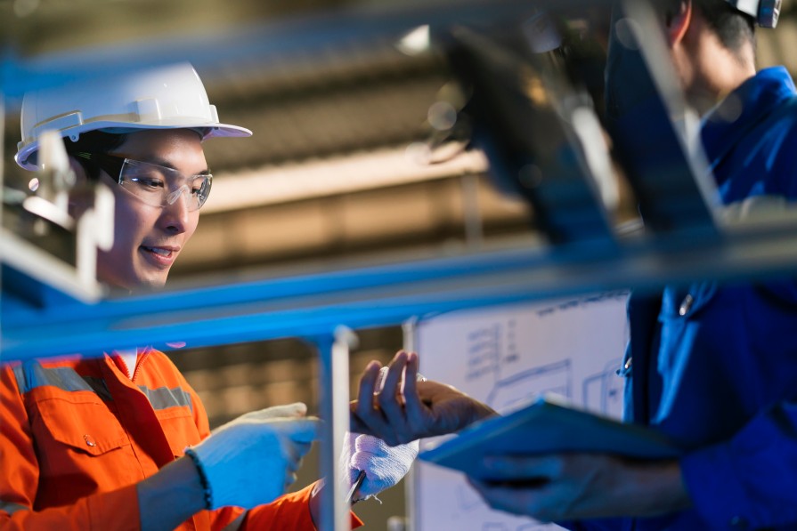 Male Asian engineer professional  having a discussion standing by the machine in the factory ,two asian coworker brainstorm explaining and solves the process curcuit mother board of the machine